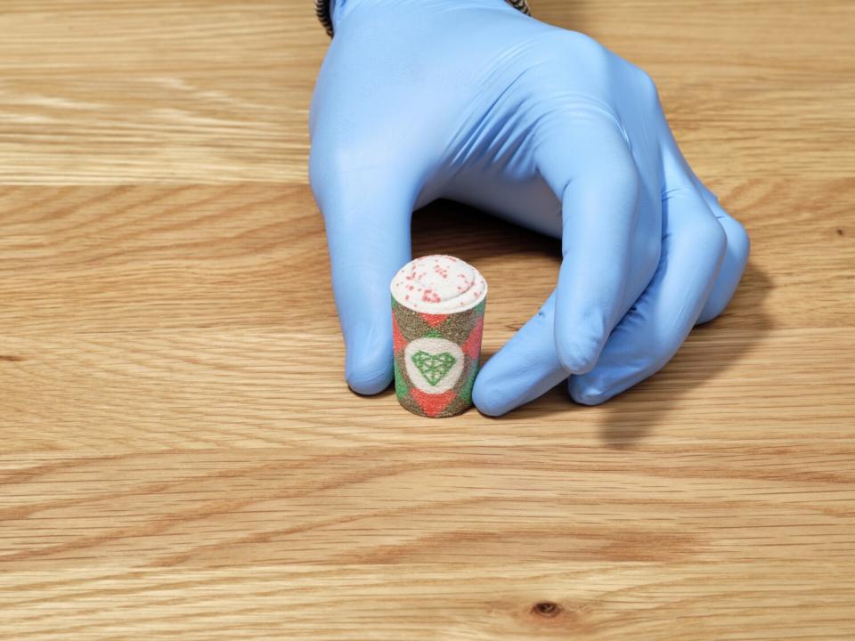 A rubber-gloved hand holds a mini latte cup made of sugar