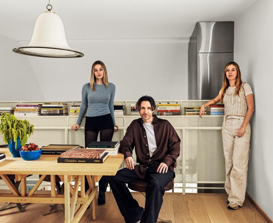 view of the kitchen dining area with three people in the photo and andre herrero is seated at the wood table and two young blond women standing behind against the counter