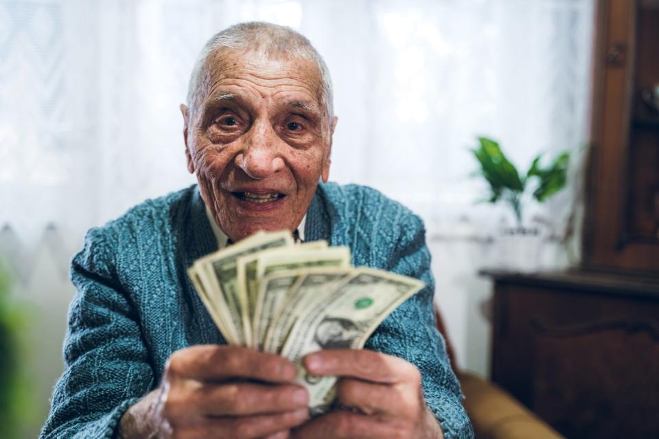 A smiling person holding an assorted pile of fanned cash bills.