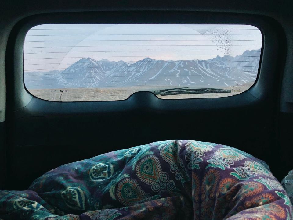 A view of the inside of the car with a colorful comforter and mountain view out the window