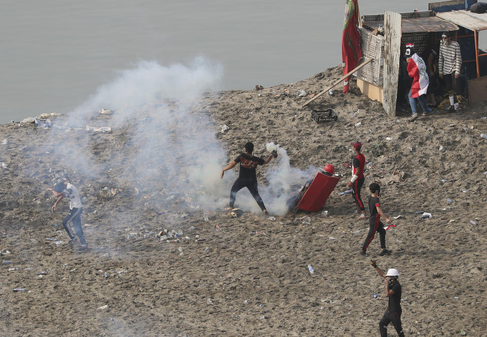 An anti-government protester prepares to throw back a tear gas canister fired by Iraq security forces to disperse a during a demonstration, in Baghdad, Iraq, Wednesday, Oct. 30, 2019. Anti-government protests in Iraq gained momentum Wednesday with tens of thousands of people gathered in a central square in Baghdad and across much of the country's Shiite-majority central southern provinces. (AP Photo/Hadi Mizban)