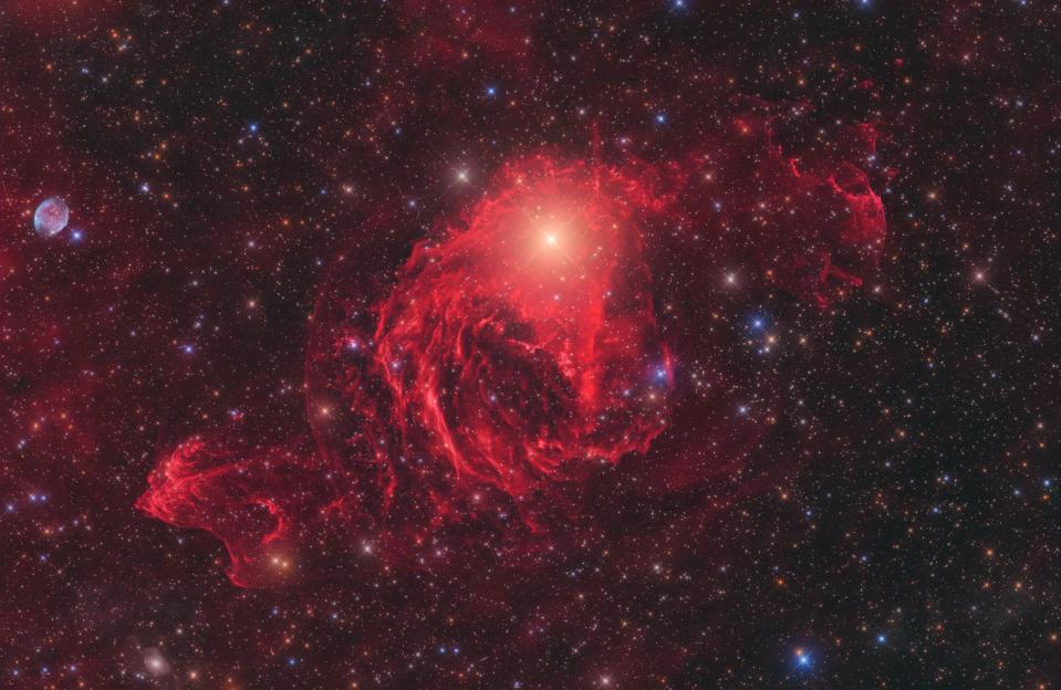 a red gaseous nebula hangs around a bright star in space.