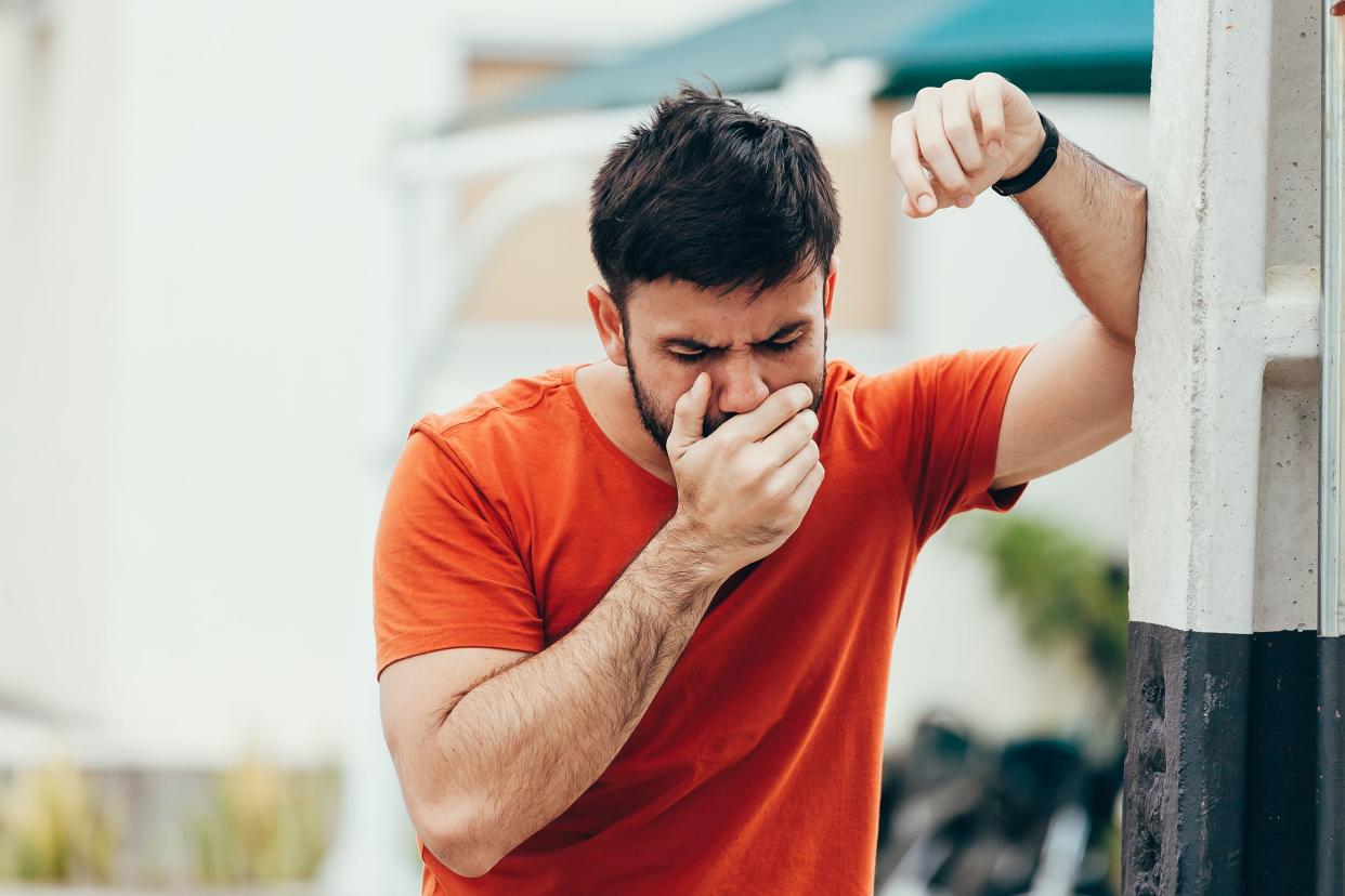 young man holding his hand over mouth to prevent vomiting outdoors