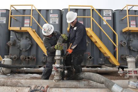 Mody Torres (L) and Josh Anderson of Select Energy Services connect hoses between a pipeline and water tanks at a Hess fracking site near Williston, North Dakota November 12, 2014. REUTERS/Andrew Cullen