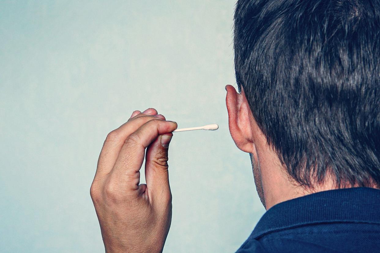 A close-up of a person holding a Q-tip, ready to stick it inside their left ear.