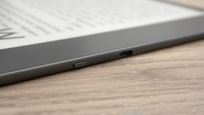 A close-up of the Kindle Scribe's sleep/wake button and USB-C port on the side of the device sitting on a wooden table.