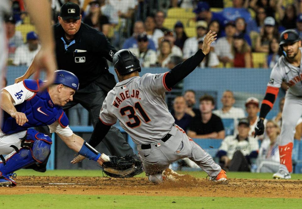 El primera base de los Gigantes, LaMonte Wade Jr., se desliza alrededor de un intento de toque del receptor de los Dodgers, Will Smith, en la octava entrada