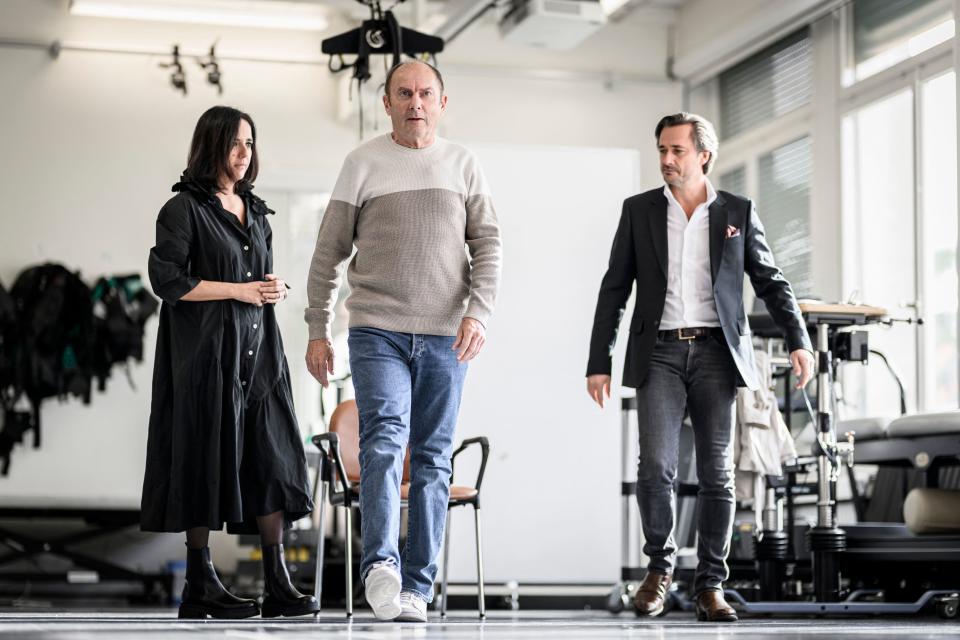 Swiss neurosurgeon, professor and co-director of NeuroRestore Jocelyne Bloch (L) and Swiss professor of neuroscience at the Swiss Federal Institute of Technology in Lausanne (EPFL) Lausanne University Hospital (CHUV) and Lausanne University (UNIL) and co-director of NeuroRestore, Gregoire Courtine (R), walk with Marc (C) a French patient suffering from Parkinson's disease fitted with a new neuroprosthesis during the presentation of a new neuroprosthesis that restores fluid walking in Lausanne, on November 3, 2023. Neuroscientists from Inserm, CNRS and the University of Bordeaux in France, together with Swiss researchers and neurosurgeons (EPFL/CHUV/UNIL), have designed and tested a 'neuroprosthesis' designed to correct the walking problems associated with Parkinson's disease. (Photo by GABRIEL MONNET / AFP) / 