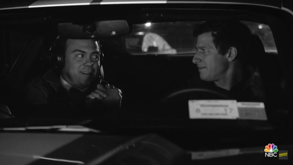 An image from Brooklyn Nine-Nine, through the windshield of a stakeout car. Charles Boyle (Joe Lo Truglia) does the brother handshake with Jake Peralta (Andy Samberg) in the driver's seat.