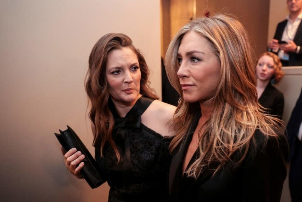 Drew Barrymore and Jennifer Aniston at an event, Barrymore holding a black clutch and wearing an off-the-shoulder dress, Aniston in a black outfit