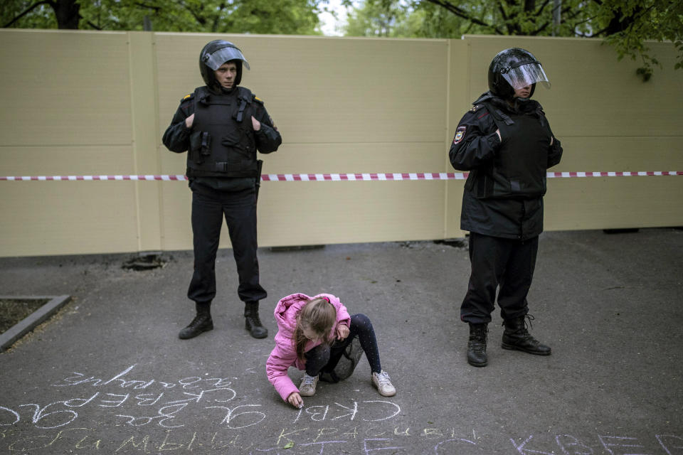 A girl writes "I'm for the park" on asphalt in front of a fence to block demonstrators protesting plans to construct a cathedral in a park in Yekaterinburg, Russia, Thursday, May 16, 2019. Russian police detained several dozen people in the early hours on Thursday at a rally protesting plans to build a cathedral in a popular park in Russia's fourth-largest city. (AP Photo/Evgeny Feldman)