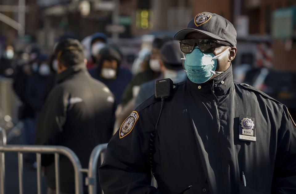 A New York City police officer wears protective gear while monitoring people waiting in line to be tested for the coronavirus outside Elmhurst Hospital in Queens on March 26. (Stefan Jeremiah / Reuters)