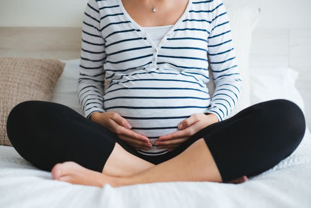 <p>iStockphoto </p> Stock image of pregnant woman sitting crosslegged, holding her bump