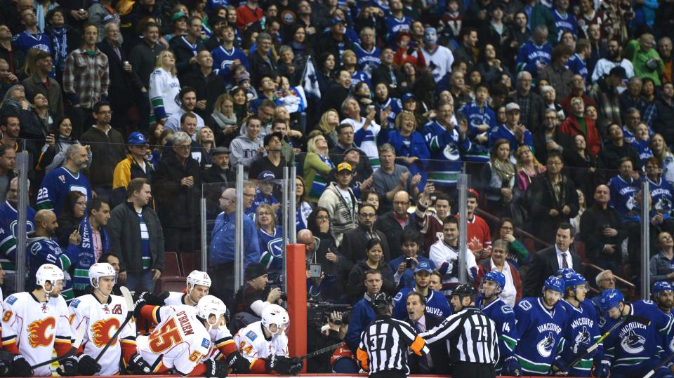 Referees get in the way of Vancouver Canucks head coach John Tortorella as he shouts at the Calgary Flames bench during first-period NHL hockey action in Vancouver, British Columbia, Saturday, Jan. 18, 2014. (AP Photo/The Canadian Press, Jonathan Hayward)