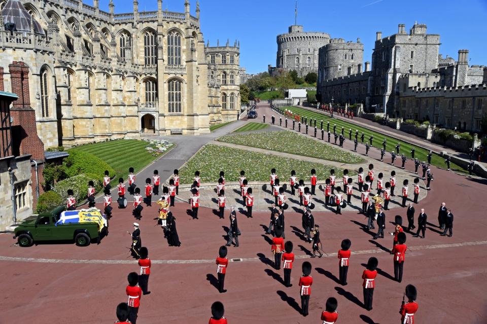 Prince Philip's coffin is at the front of a procession while military members in red coats and bearskin hats stand nearby.