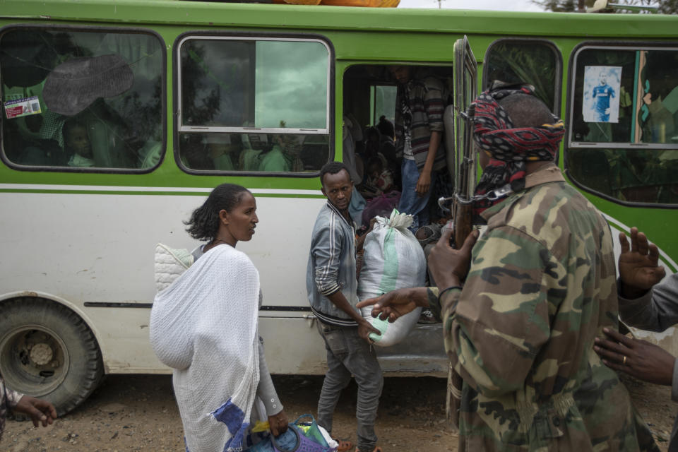 People prepare to depart on a bus as a fighter loyal to the Tigray People's Liberation Front (TPLF), right, stands guard in the town of Hawzen, then-controlled by the group, in the Tigray region of northern Ethiopia, on Friday, May 7, 2021. While the government now holds many urban centers, fierce fighting continues in remote rural towns like Hawzen. (AP Photo/Ben Curtis)