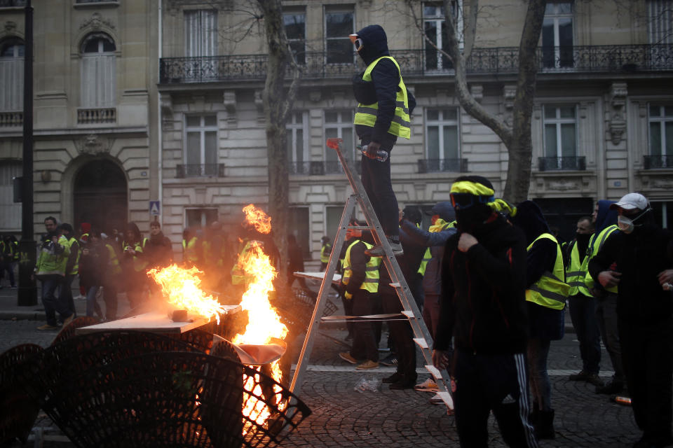 A demonstrator stands on a stepladder during clashes Saturday, Dec. 8, 2018 in Paris. Crowds of yellow-vested protesters angry at President Emmanuel Macron and France's high taxes tried to converge on the presidential palace Saturday, some scuffling with police firing tear gas, amid exceptional security measures aimed at preventing a repeat of last week's rioting. (AP Photo/Rafael Yaghobzadeh)