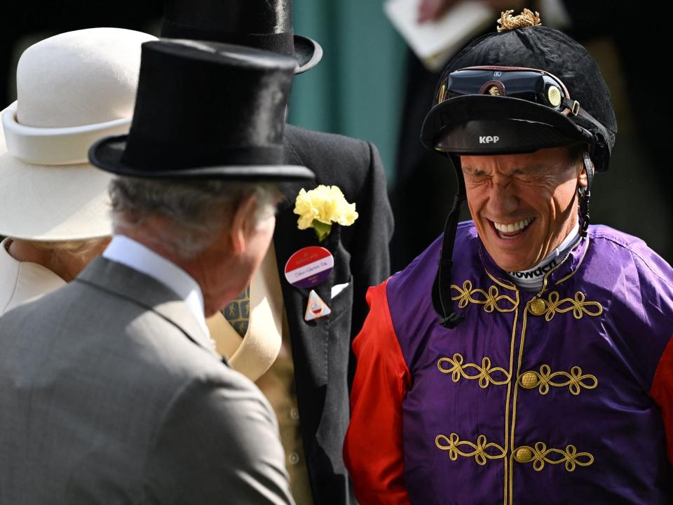 Lanfranco Dettori laughing and wearing a purple and red outfit while standing next to King Charles and Queen Camilla.