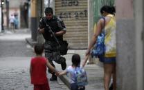 A police officer takes up position during an operation at the Mare slums complex in Rio de Janeiro March 25, 2014. Brazil will deploy federal troops to Rio de Janeiro to help quell a surge in violent crime following attacks by drug traffickers on police posts in three slums on the north side of the city, government officials said on Friday. Less than three months before Rio welcomes tens of thousands of foreign soccer fans for the World Cup, the attacks cast new doubts on government efforts to expel gangs from slums using a strong police presence. The city will host the Olympics in 2016. REUTERS/Ricardo Moraes (BRAZIL - Tags: CRIME LAW)