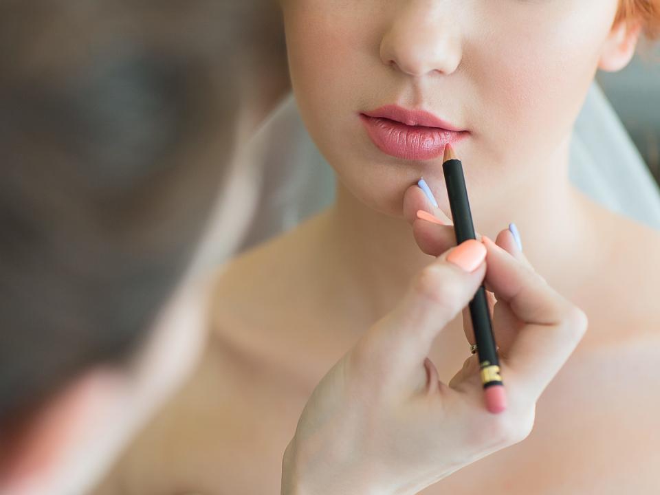 Makeup artist lines client's lips with a pink lip liner