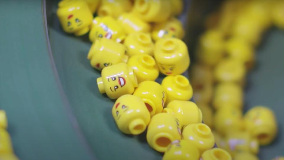 A collection of yellow LEGO minifigure heads in a drum at the factory