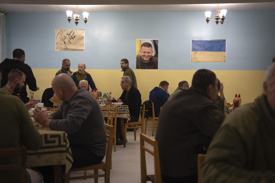 Wounded soldiers, including a group of Colombian army veterans who joined the Ukrainian armed forces to help the country fight Russia, have lunch in a hospital in Ukraine on Wednesday, Dec. 20, 2023. A portrait of the commander-in-chief of Ukraine's armed forces is in the background. After two years of war, Ukraine is looking for ways to replenish its depleted ranks, and the Colombian army volunteers are a welcome addition. (AP Photo/Efrem Lukatsky)