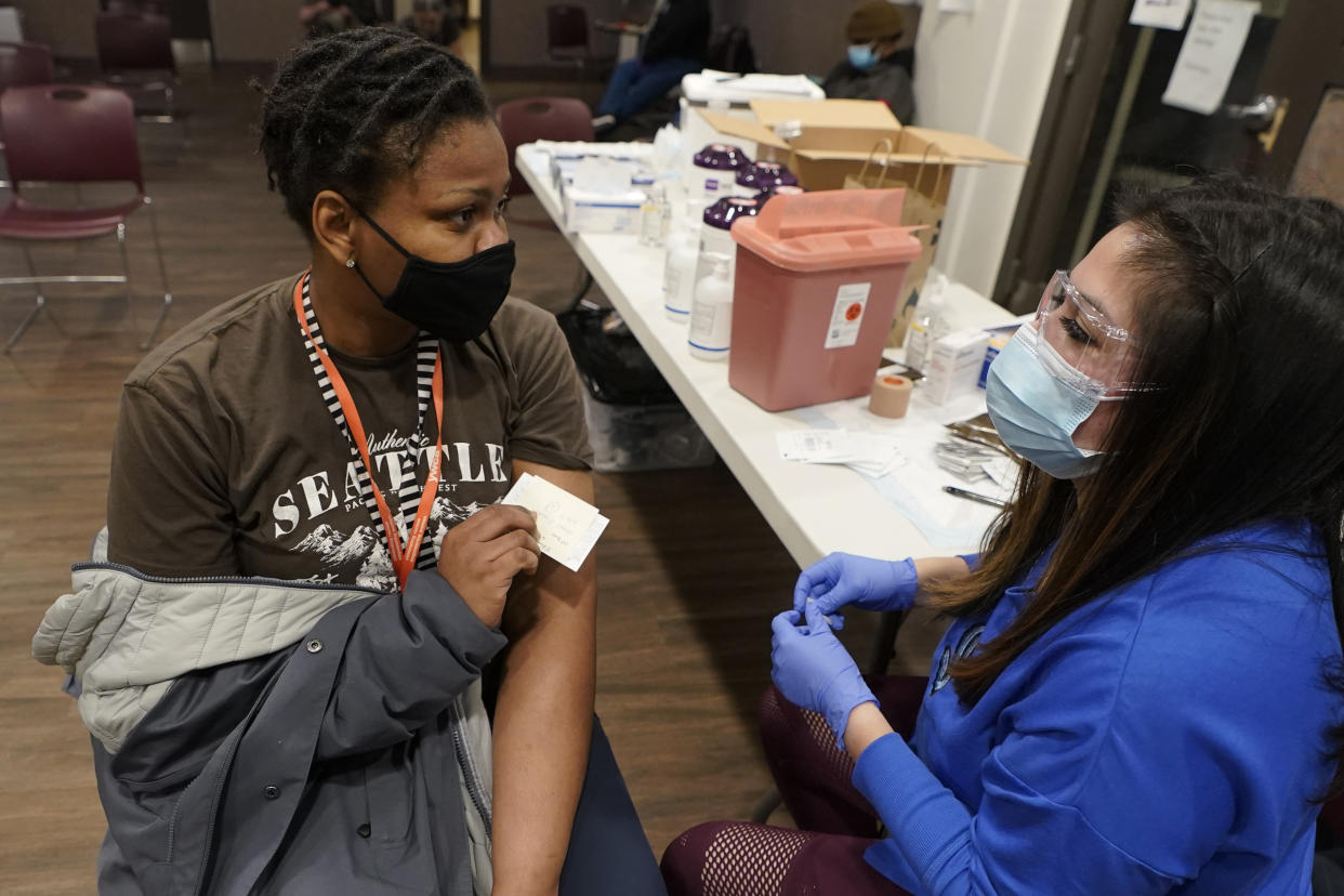 Judy Jideonwo, left, a case manager at Angeline's Day Center For Women, which is part of a YWCA shelter for women lacking housing in Seattle, holds her vaccination card after she received the first dose of the Moderna COVID-19 vaccine, Wednesday, April 7, 2021, from Aurora Artman, right, a medical assistant at Harborview Medical Center, at a vaccination clinic set up at the shelter. Advocates say homeless people are at greater risk of being infected and greater risk of hospitalization and death than the average person, and they should have been prioritized earlier. (AP Photo/Ted S. Warren)