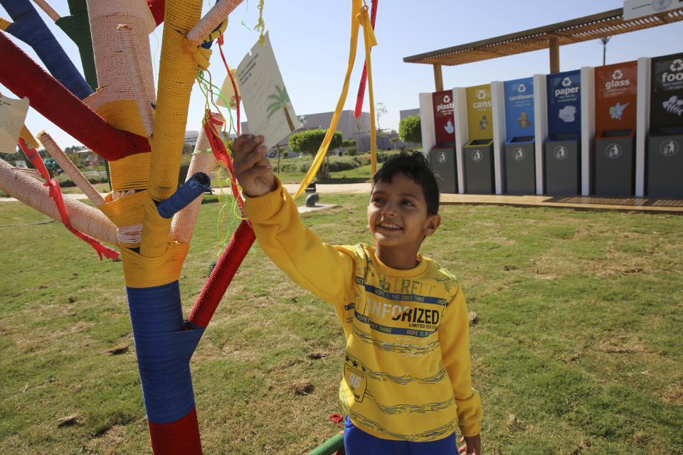 An Egyptian boy reads a note posted on an artificial tree set up for people to hang a note saying what promise they will make to help fight climate change, in the Green Zone of the COP27 U.N. Climate Summit, in Sharm el-Sheikh, Egypt, Friday, Nov. 18, 2022. (AP Photo/Thomas Hartwell)