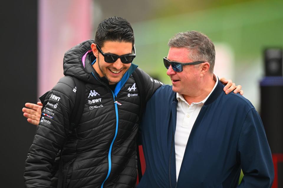 formula 1 driver esteban ocon and commentator david croft stand in the paddock with their arms around each other