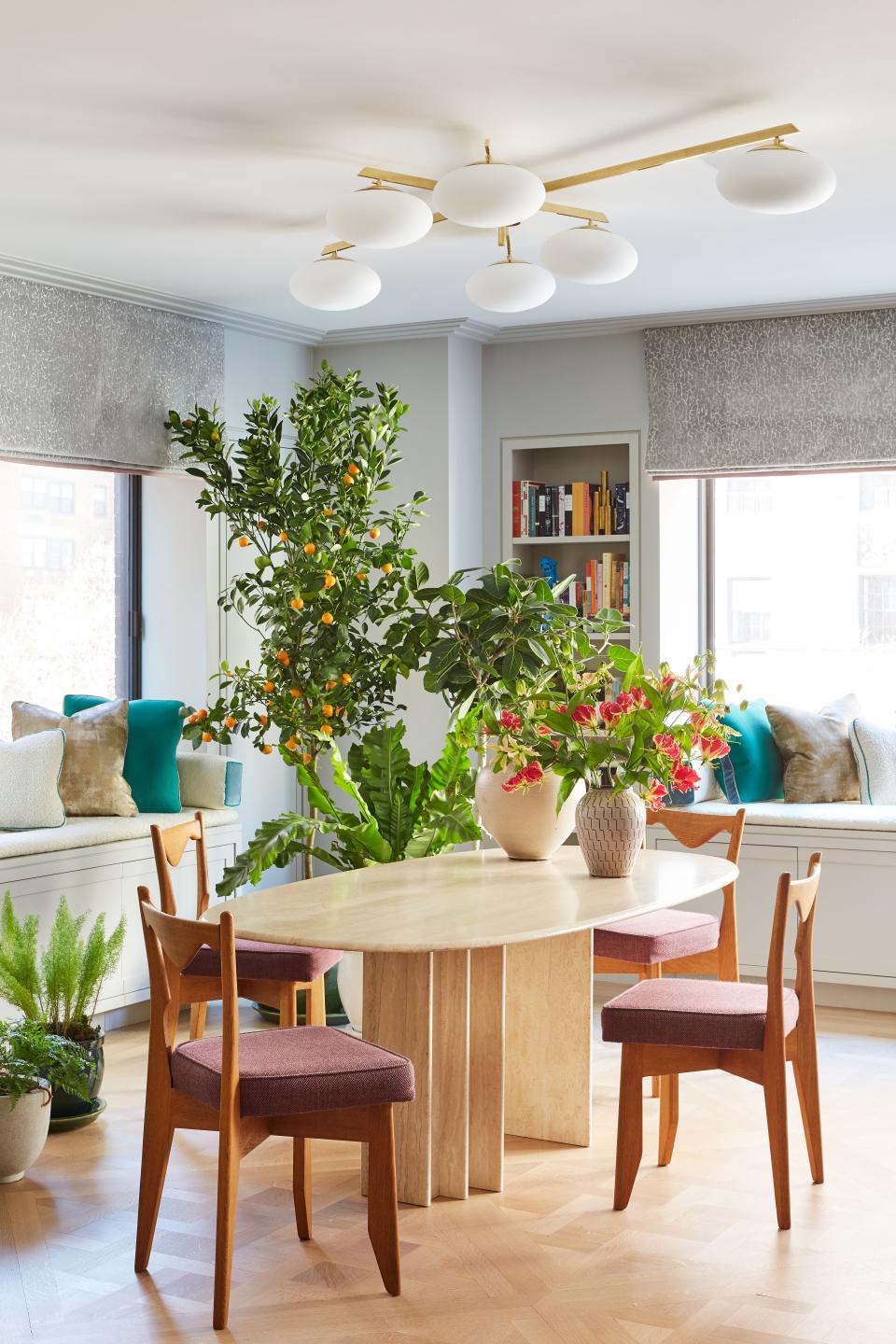 The dining room, which is in the former living room, features a ’70s Italian travertine table from the Paris flea market. Oak dining chairs are by Guillerme et Chambron from Maison Gerard. The mod ceiling fixture is by Angelo Lelli from a gallery in Paris. Roman shades and window seats are found throughout the house, covered in fabrics from Angela Brown Ltd., Mood, Sabina Fay Braxton, Manuel Canovas, and Donghia.