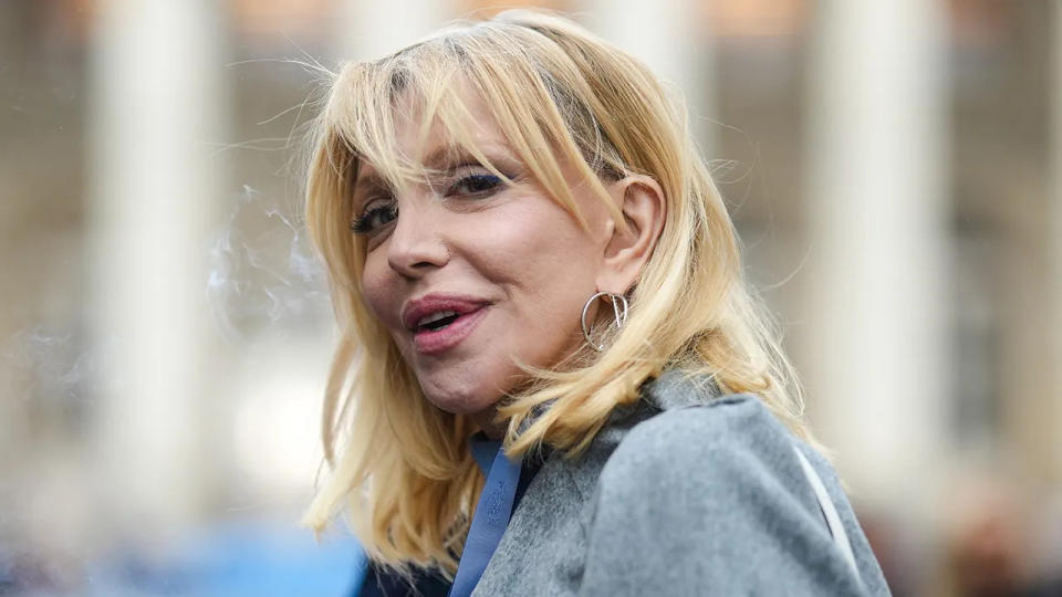 Courtney Love in a jean jacket looks towards the camera as she walks in Paris