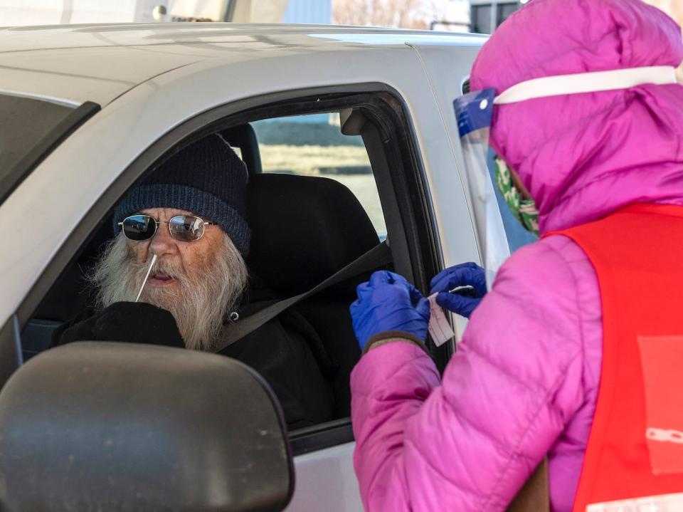 man at drive-thru testing site performs binaxnow rapid test on himself, as attendant waits at his window