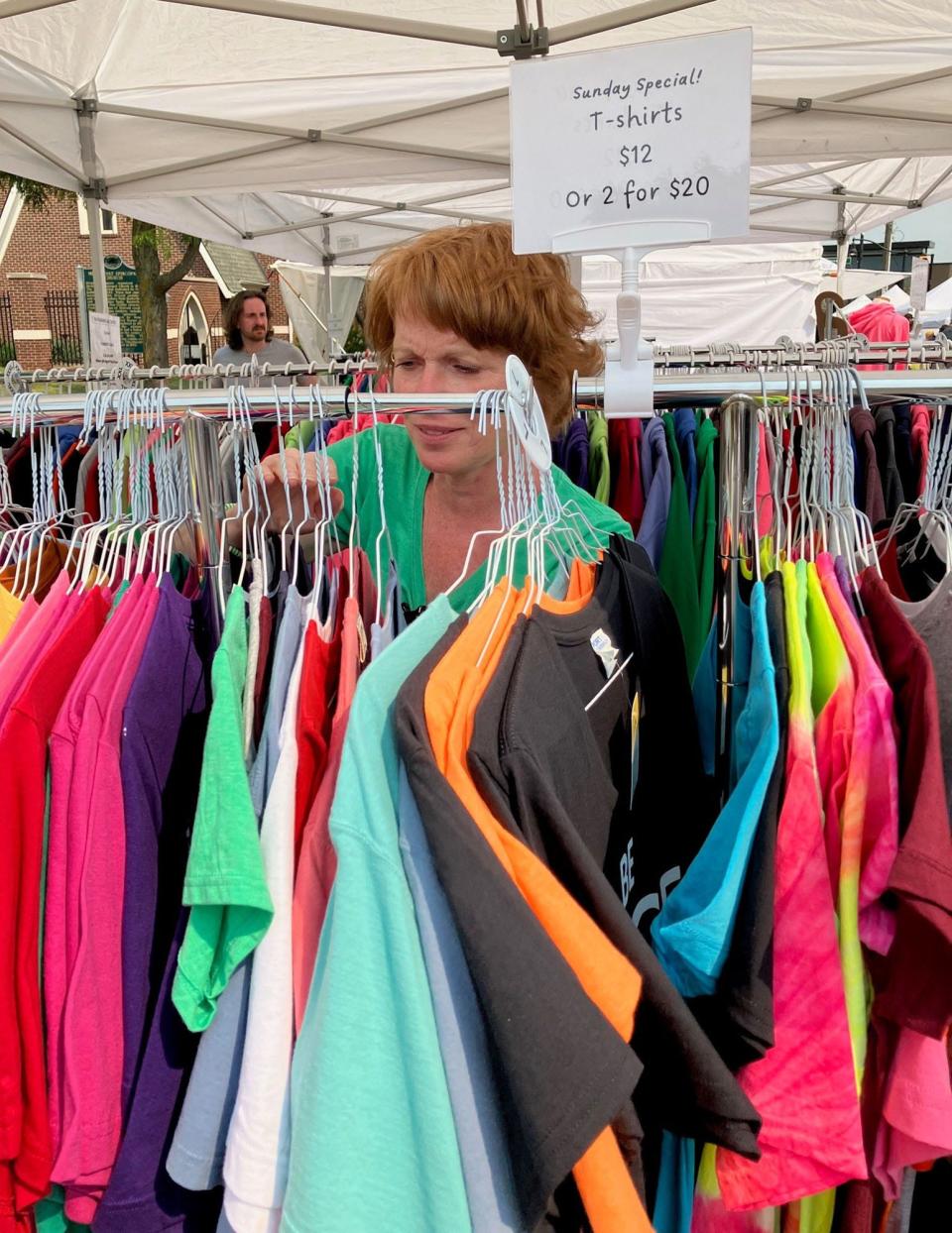 Mary Keyser hangs T-shirts at a booth at Art on The Grand in downtown Farmington on Sun., June 4. The T-shirts are among the items with positive messages that she sells to raise money to perform random acts of kindness.