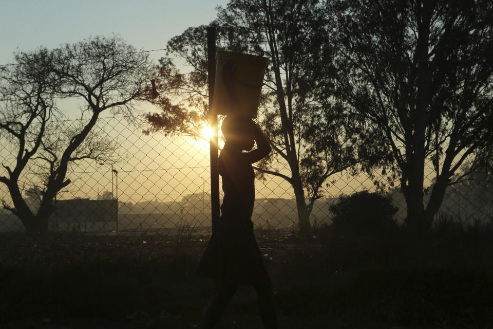 A young girl carries a bucket of water after fetching it from a borehole in Harare, Thursday, Aug, 8, 2019. The sight of Harare residents walking home at dusk carrying firewood and water buckets has become common as the country struggles with water and power crisis.(AP Photo/Tsvangirayi Mukwazhi)