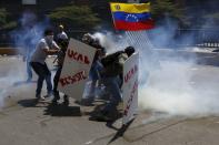 Un grupo de manifestantes opositores al gobierno de Nicolás Maduro se ocultan detrás de las pancartas marcadas con las siglas de la Universidad Católica Andrés Bello, mientras la policía los ataca con bombas lacrimógenas este jueves 20 de marzo de 2014 en Caracas, Venezuela. REUTERS/Carlos Garcia Rawlins