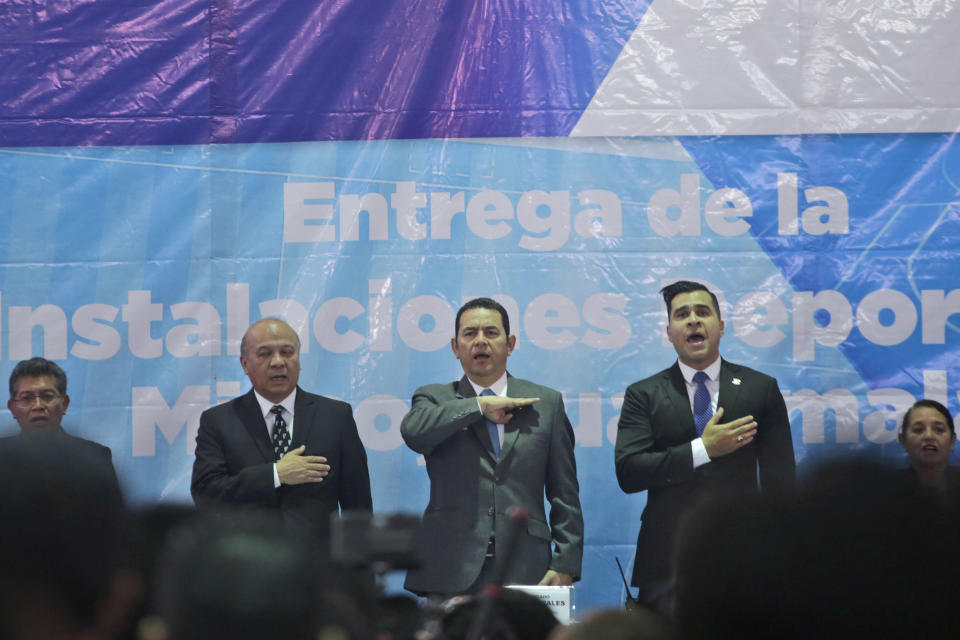 Guatemalan President Jimmy Morales, center, sings the national anthem, acompanied by Mixco mayor Ernesto Bran, right, and Culture Minister Jose Chex, during the inauguration of a soccer field in Mixco, Guatemala, Monday, Sept. 17, 2018. Morales' government will defy a ruling by the country's top court and block the return of Ivan Velasquez, who is leading a U.N.-backed anti-corruption commission. (AP Photo/Moises Castillo)