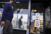 A pedestrian in a mask passes shuttered storefronts on Thursday, Oct. 15, 2020, as restrictions are imposed on the area due to an increase in COVID-19 infections in the Far Rockaway neighborhood of the borough of Queens in New York. After shutdowns swept entire nations during the first surge of the coronavirus earlier this year, some countries and U.S. states are trying more targeted measures as cases rise again around the world. (AP Photo/John Minchillo)