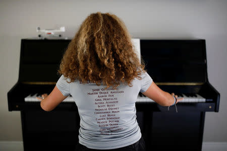 Daniela Menescal, who was injured by shrapnel during the mass shooting at Marjory Stoneman Douglas High School, wears a t-shirt with the names of the victims of the shooting, as she plays the piano at her house in Parkland, Florida, U.S., April 4, 2018. REUTERS/Carlos Garcia Rawlins