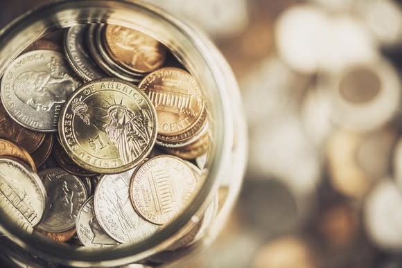 Coin jar resting on top of  a pile of coins.