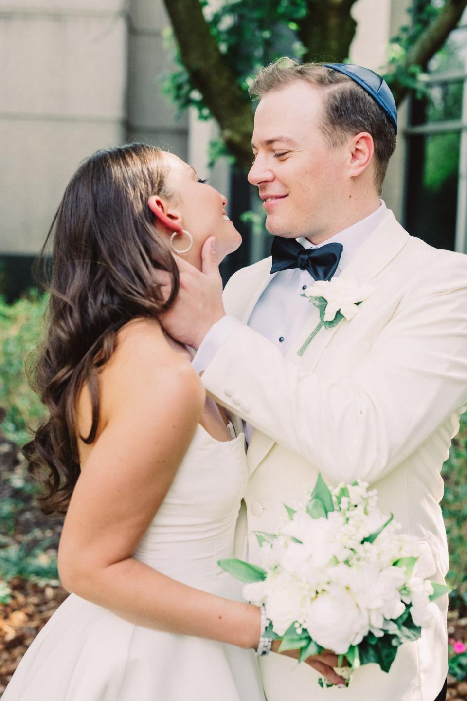 A groom holds his bride's face and smiles at her.