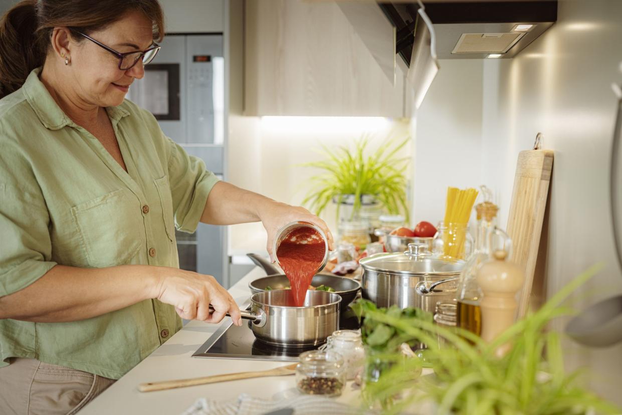 Woman pouring tomato sauce from a can to a saucepan