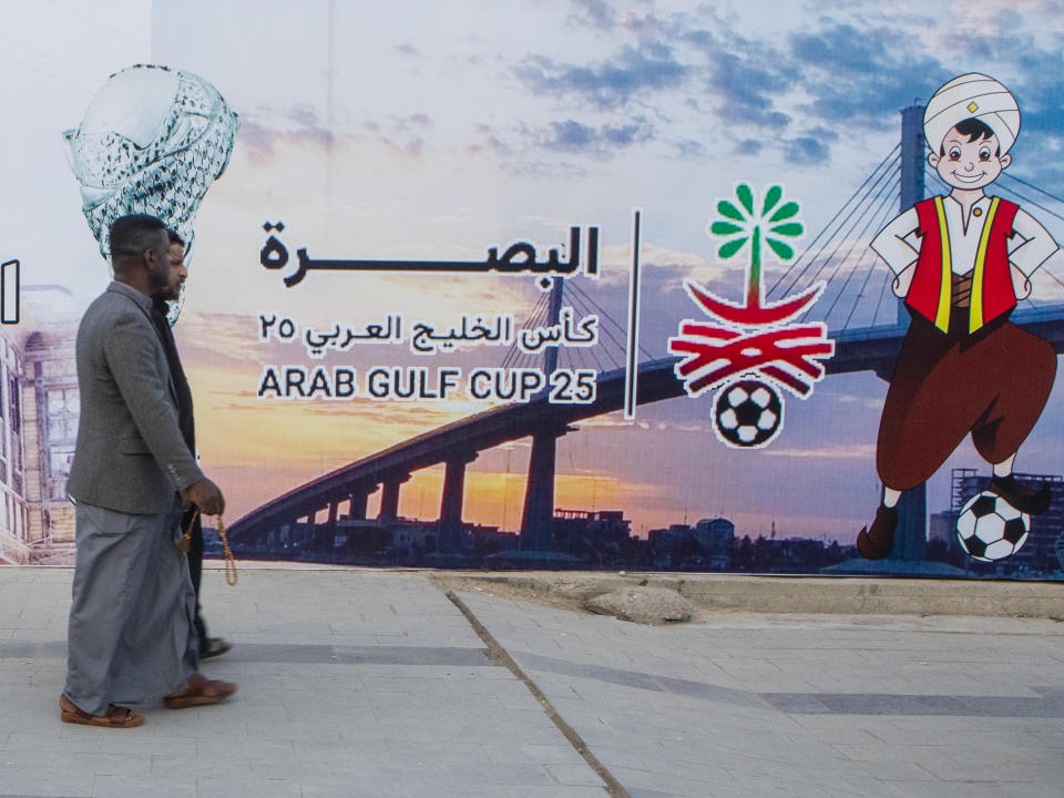 People pass by a billboard announcing Arab Gulf Cup in Basra, Tuesday, Jan. 3, 2023. The 25th edition of the Arabian Gulf Cup will be held in the city of Basra, the first time the turmoil-wracked country will host the tournament since 1979. (AP Photo/Nabil al-Jurani)i)