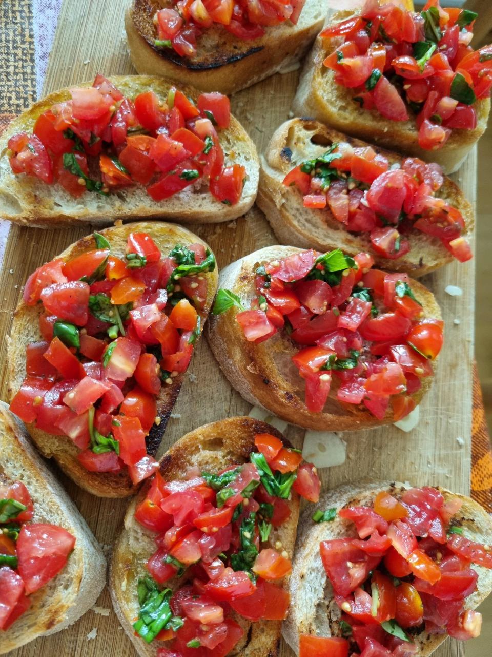 Bruschetta topped with diced tomatoes and basil on a wooden cutting board