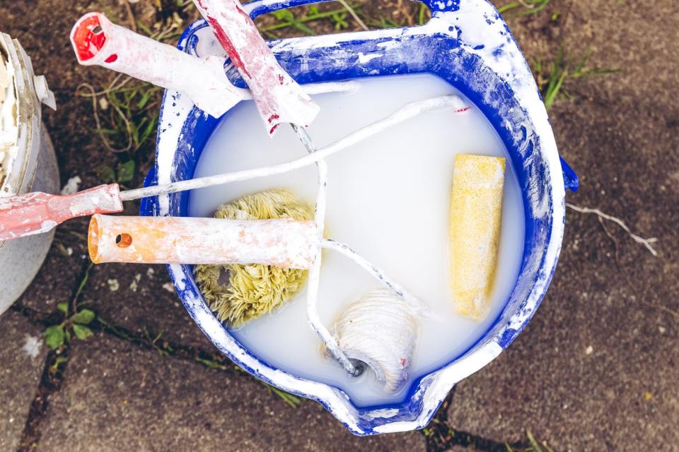 Soaking paint rollers in a blue bucket filled with water.