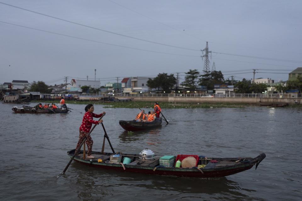 Nguyen Thi Thuy, a vendor who sells steamed buns on a floating market, paddles her boat near a few tourist boats navigating the market in Can Tho, Vietnam, Wednesday, Jan. 17, 2024. On good days she makes about $4 — hardly enough to put food on the table. (AP Photo/Jae C. Hong)