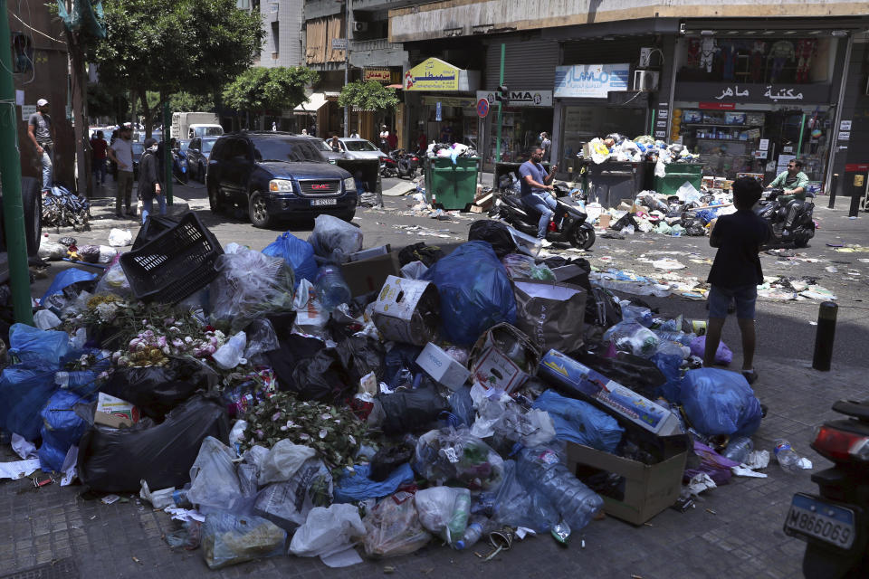 FILE - In this July 14, 2020 file photo, a road is partially blocked with garbage and bins in protest of uncollected trash, in Beirut, Lebanon. Lebanon is hurtling toward a tipping point at an alarming speed, driven by financial ruin, collapsing institutions, hyperinflation and rapidly rising poverty _ with a pandemic on top of that. The collapse threatens to break a nation seen as a model of diversity and resilience in the Arab world. (AP Photo/Bilal Hussein, File)