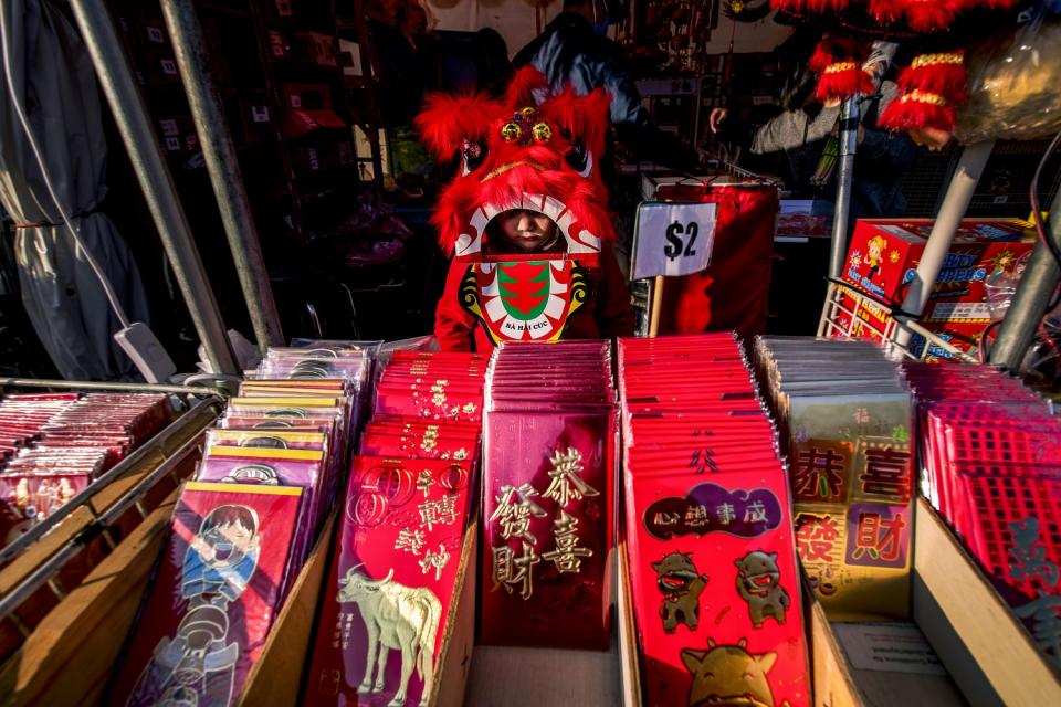 A girl peers out from her lion dance costume while looking over rows of red money envelopes.