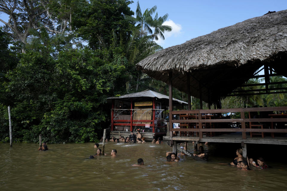 A family bathes in the waters of the Igarape Combu in front of a restaurant on the shores of Ilha do Combu, near the city of Belem, Para state, Brazil, Sunday, August 8, 2023. (AP Photo/Eraldo Peres)