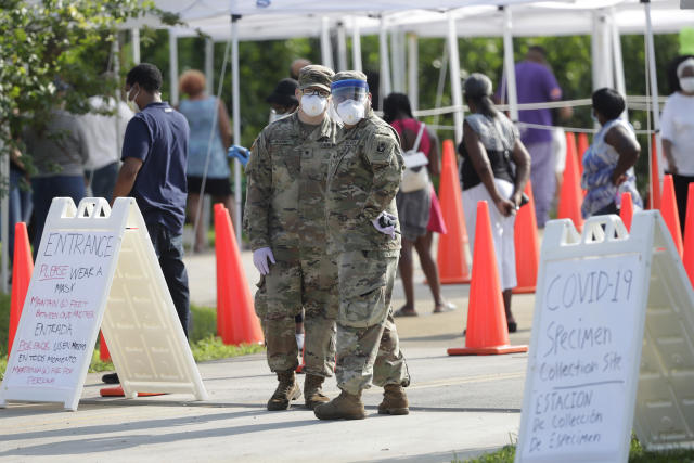National Guardsmen look on as people wait in line at a walk-up coronavirus testing site during the COVID-19 pandemic, Saturday, April 18, 2020, at the Urban League of Broward County in Fort Lauderdale, Fla. (AP Photo/Wilfredo Lee)