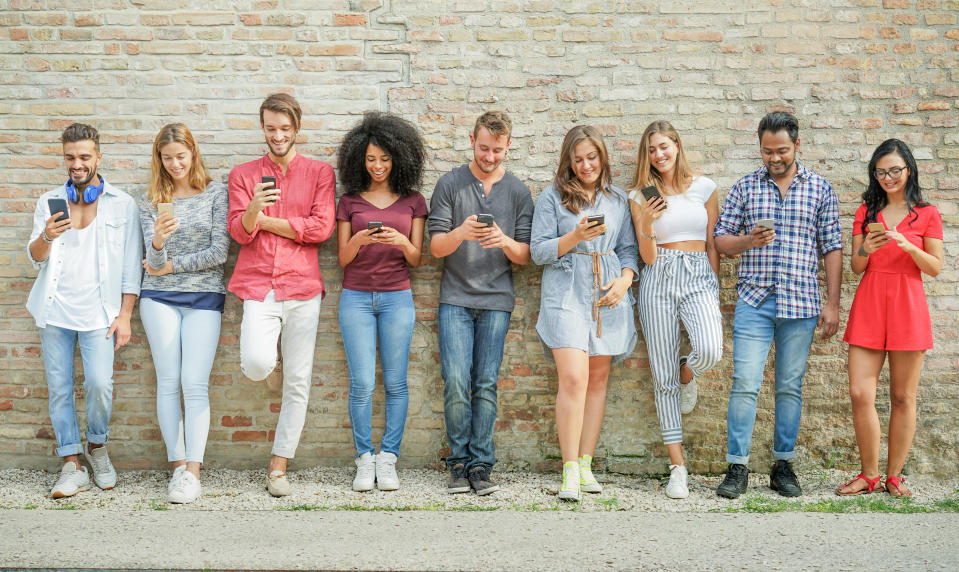 A group of people using their smartphones in front of a brick wall.